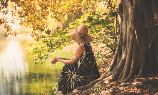 A young woman is sitting under a tree by the river